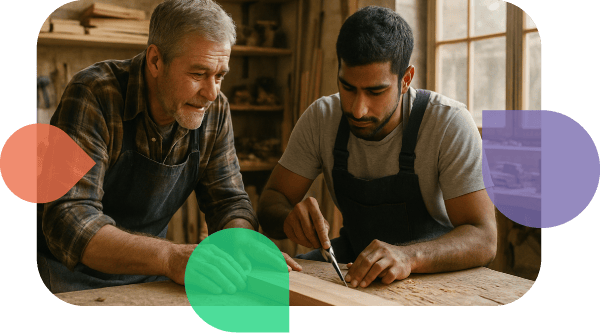 Ein Tischlermeister leitet einen jungen Auszubildenden in einer Holzwerkstatt an. Das Bild des Welcome and Work Centers Landkreis Osnabrück steht für die gelungene Ausbildung, Integration und Arbeitsmarktintegration im Handwerk des Osnabrücker Landes.